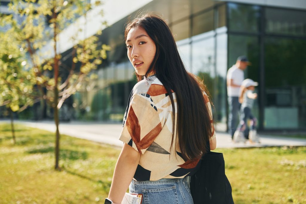 Student walks near modern building. Young asian woman is outdoors at daytime