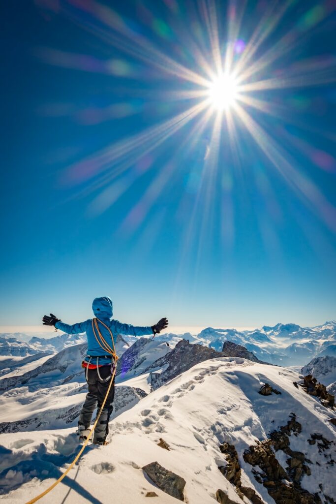 man in blue jacket and black pants standing on snow covered mountain under blue sky during